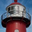 Close-up van een rood-witte vuurtoren met lantaarn en balustrade