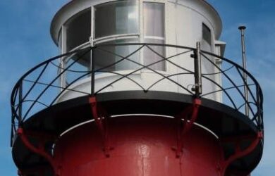 Close-up van een rood-witte vuurtoren met lantaarn en balustrade